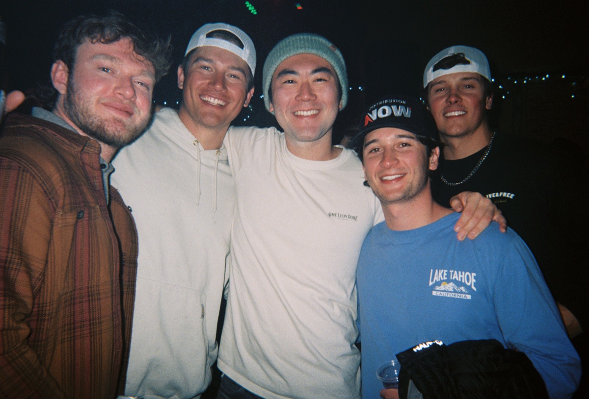 Five friends posing together at night in casual clothes and hats
