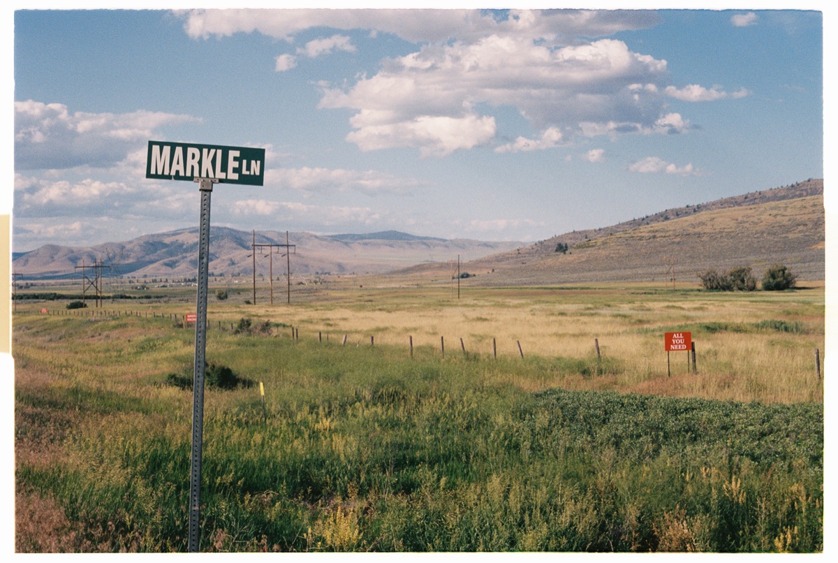 Rural road sign reading Markle Ln with open grassland and mountains under blue sky