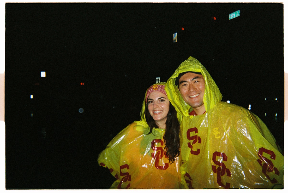 Two people smiling in yellow USC rain ponchos at night