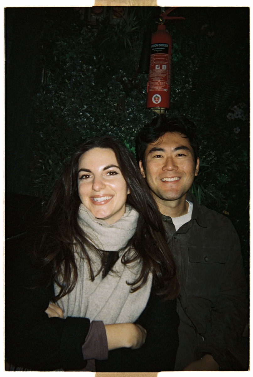 Couple smiling together in front of a green wall at night