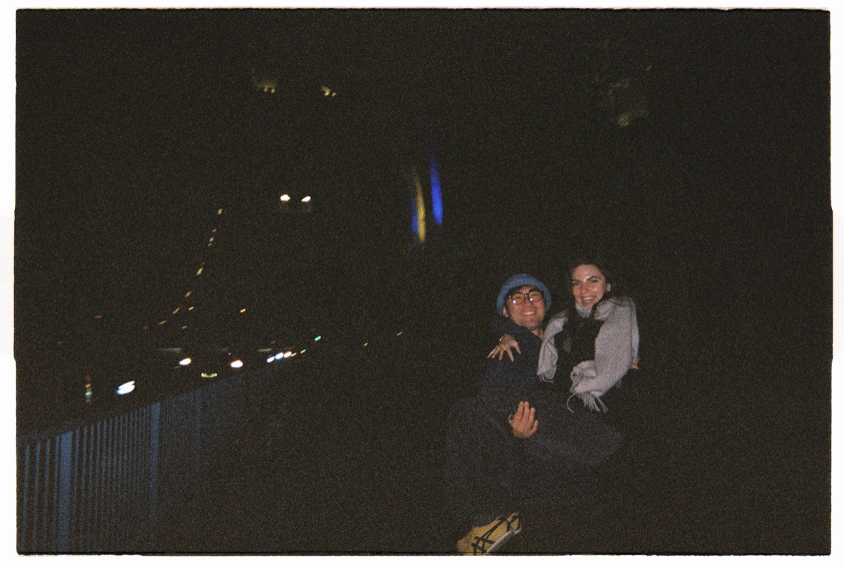Two friends sitting together on a city bridge at night