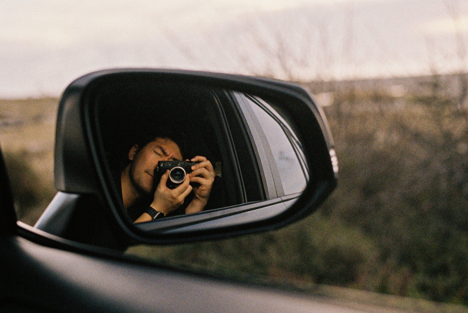 Self-portrait in side mirror with film camera