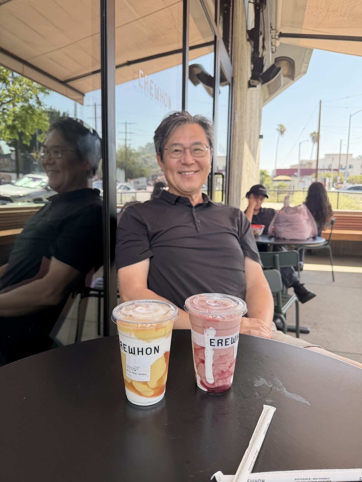 Kevin's dad smiling at an outdoor Erewhon table with two smoothies in front of him